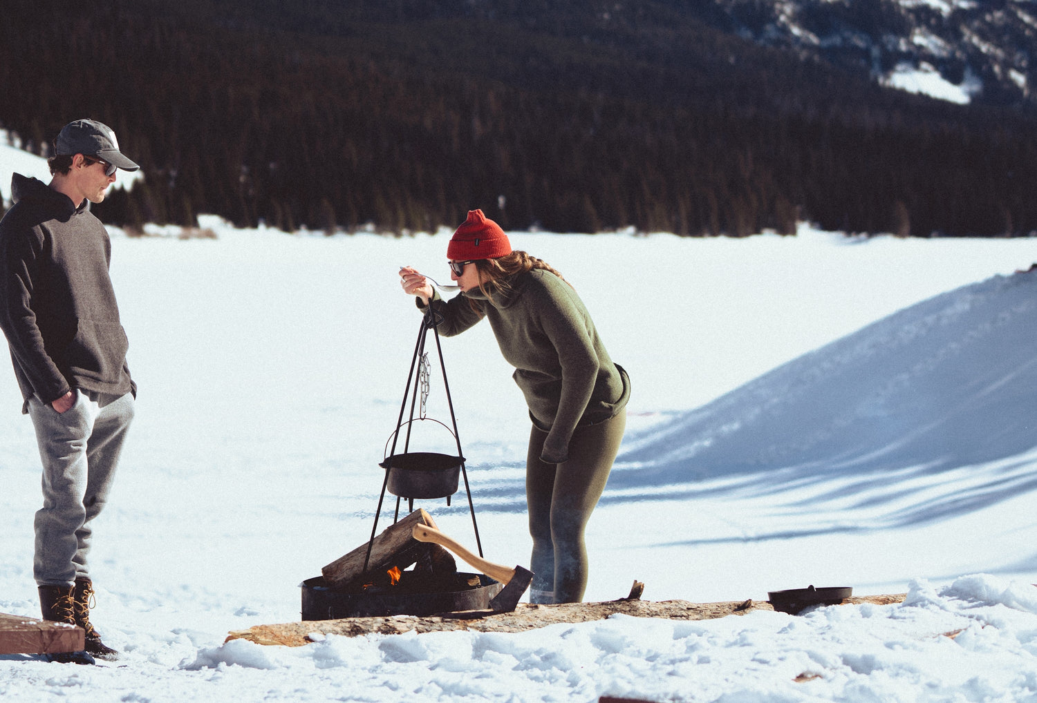 A couple cooking around a fire in the snow.