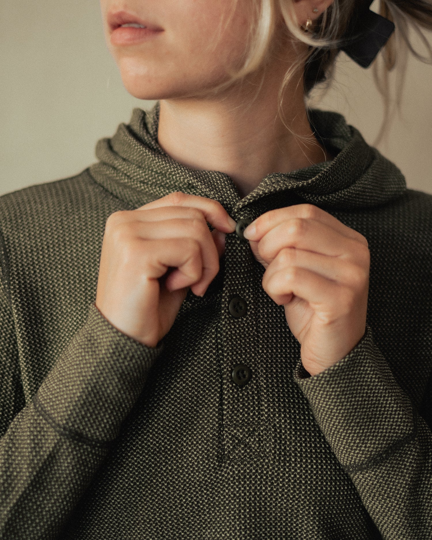 A woman buttons the top button of her merino wool waffle knit henley.